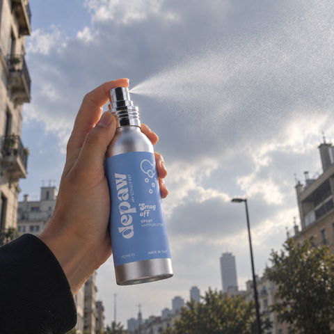 Mano che vaporizza lo spray Smog Off verso il cielo tra i palazzi di una città
